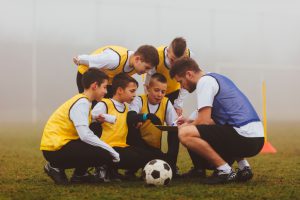 Children playing soccer. They are having training with their coach on foggy, cold, winter morning. They are dedicated to become a new soccer stars. Everybody kneeling and coach giving them instructions. Sketching on notepad. Shot with Canon EOS 5Ds.